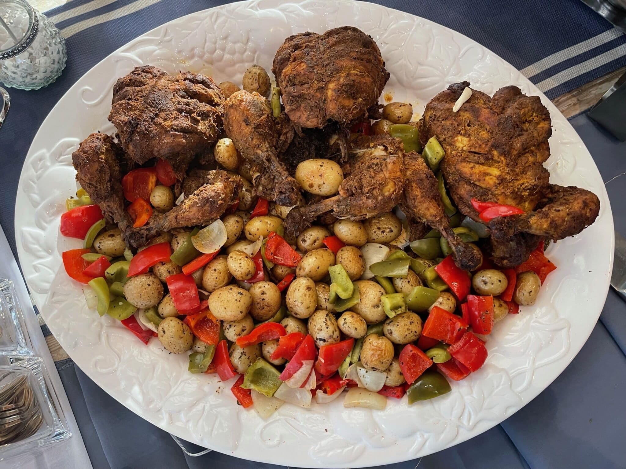 A large white platter of roasted halal chicken pieces mounded over baby potatoes tossed with red and green bell peppers and onions, from the Ladle n Wok kitchen.
