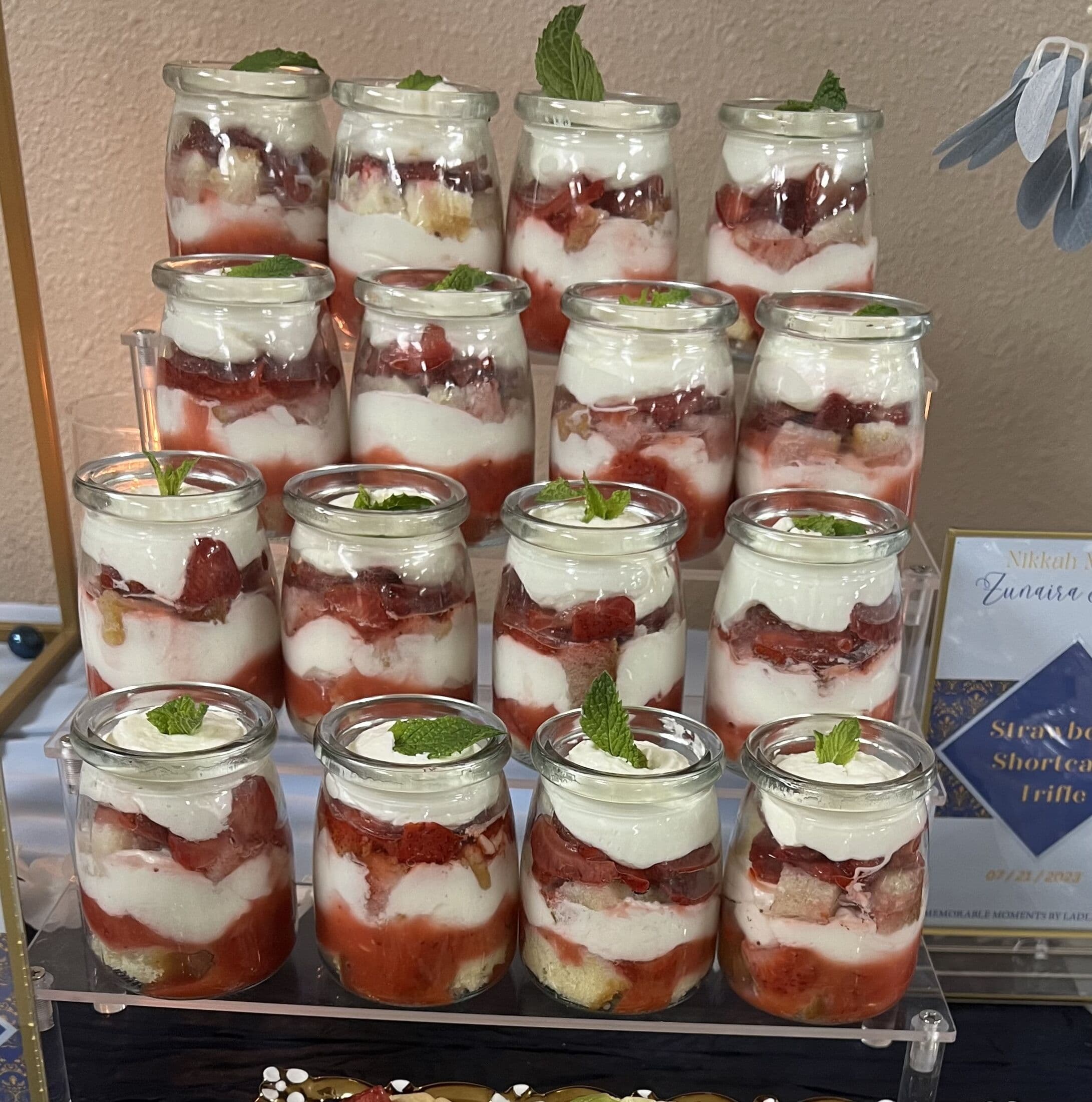 Individual strawberry shortcake trifles layered with cream, sponge and macerated strawberries in glass jars, each topped with a mint leaf and tiered on a stand at a Bay Area Nikkah.
