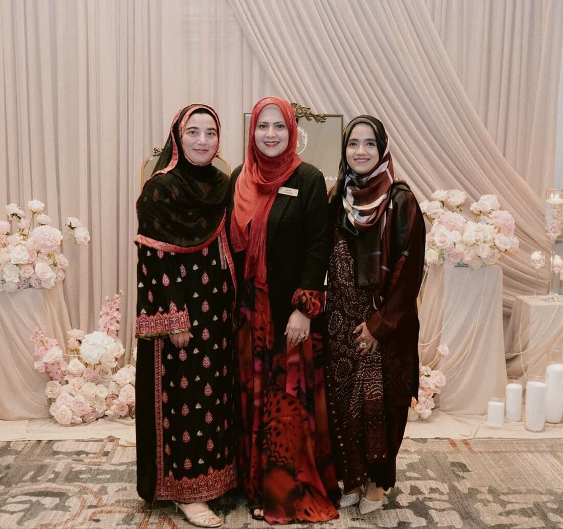 Arifa, Sarah and Tabassum, the founders of Memorable Moments by Ladle n Wok, standing together in front of a blush draped backdrop with rose arrangements.